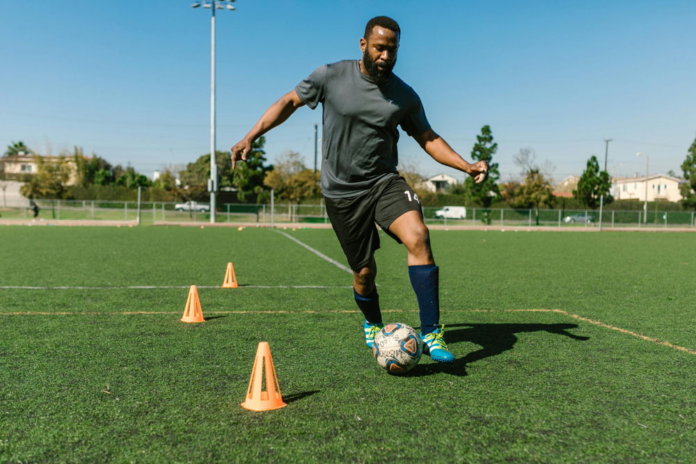 Footballers Community | A Football player dribbling the ball around cones during training.